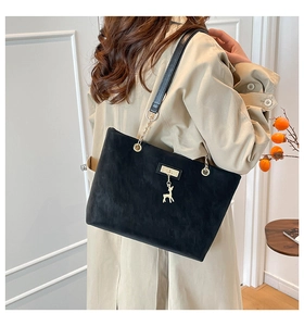 Close-up of black matte tote bag with gold deer pendant and chain strap on a model