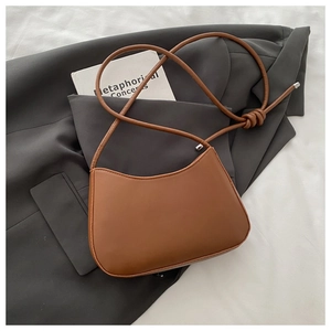Flat lay of caramel leather shoulder bag with knotted strap on a grey suit jacket