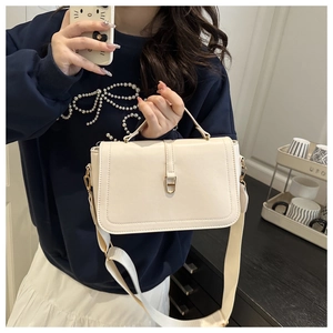 Close-up of a white leather crossbody bag with wide strap and gold metal clasp