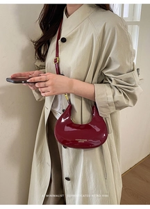 Dettaglio della borsa a mezzaluna in vernice bordeaux indossata con un trench beige elegante