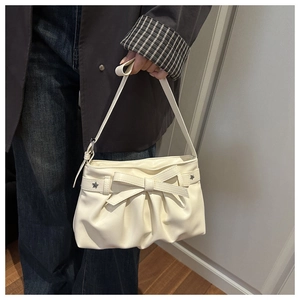 Detail of cream white pleated shoulder bag featuring a large bow and star metal charm