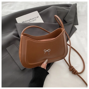 Detail of a brown leather crescent bag featuring a silver metal bow and knotted strap
