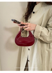 Dettaglio della modella che tiene la borsa a mezzaluna in pelle verniciata bordeaux