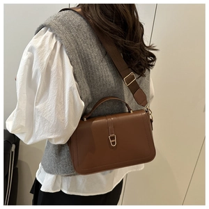 Brown crossbody bag with wide strap worn by a model in a minimalist setting