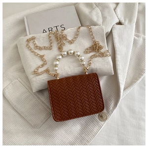 Detailed close-up of brown woven crossbody bag with pearl handle and golden chain strap
