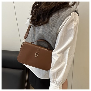Detail of a dark brown leather shoulder bag featuring elegant gold clasp and top handle