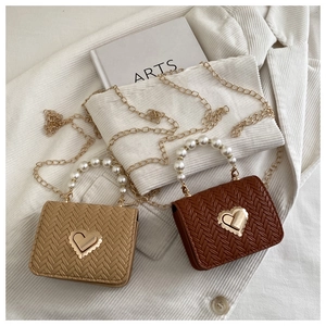 Close-up of pearl handle and golden heart lock on woven mini crossbody bags