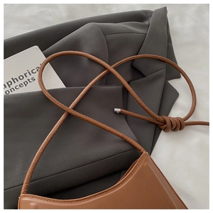 Detailed macro view of matte leather shoulder bag with circular knotted strap design