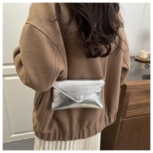 Silver envelope clutch bag with gold chain strap shown on model's shoulder in interior