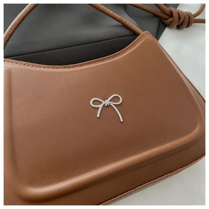 Close-up of caramel brown leather shoulder bag with silver metal bow detail and fine stitching