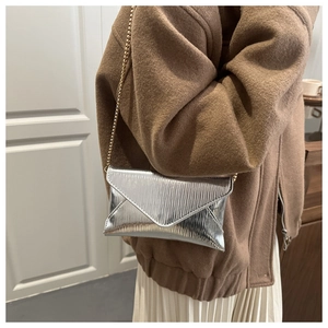 Detail of silver metallic envelope bag with vertical pleated texture and gold chain strap
