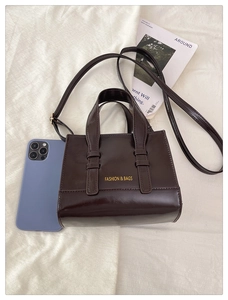 Flat lay of dark brown leather tote bag with yellow logo and shoulder strap detail