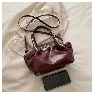Detail of burgundy ruched tote bag with glossy finish and elegant gold buckle closure