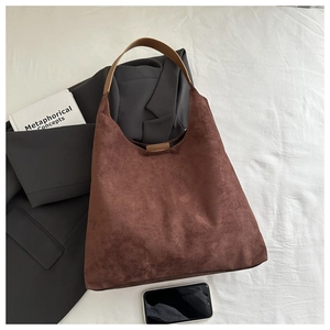 Detail of a large brown suede tote bag with wide strap on a minimalist studio backdrop