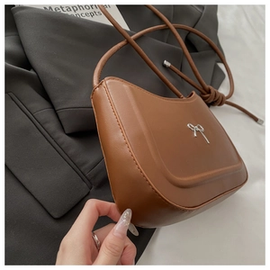 Detail of a brown leather half-moon bag with a silver bow buckle and knot strap design