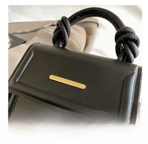 Detail of black leather handbag featuring a gold metal bar and twisted knot handle