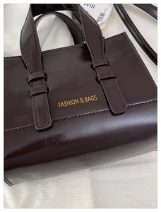 Detail of deep brown tote bag featuring glossy oil leather texture and gold metal accents