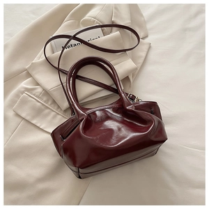 Detail view of burgundy tote bag with pleats and adjustable shoulder strap on suit jacket