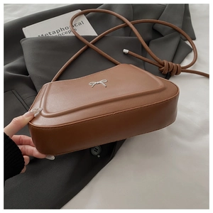 Detail of a brown matte leather bag featuring a silver metal bow and knotted shoulder strap