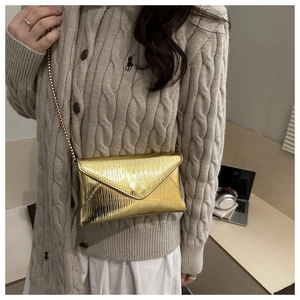 Detail of gold metallic envelope crossbody bag with textured finish and chain strap