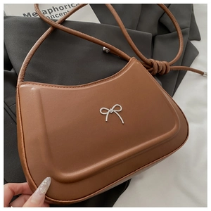Detail of caramel brown shoulder bag featuring a silver bow accent and knotted strap detail