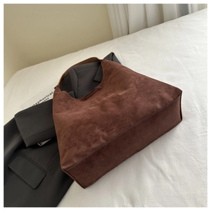 Detail of a brown matte suede tote bag resting on a gray blazer for a casual commute look