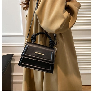 Detail of minimalist black crossbody bag with knotted handle on trench coat