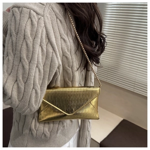 Detail of gold envelope crossbody bag with vertical pleated texture and metal chain strap