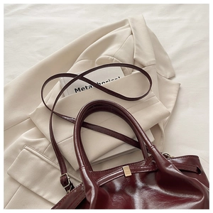 Close-up of deep wine red glossy leather bucket bag with gold hardware and strap
