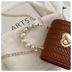 Detail of woven brown leather bag with pearl handle and golden heart twist lock