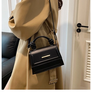 Close-up of black PU leather handbag with gold metal bar and unique knotted top handle design