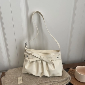 Elegant beige bow tote bag with star rivets and pleated base on a cozy knitted blanket