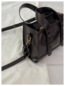 Detail view of coffee brown patent leather mini tote bag with adjustable strap and gold logo