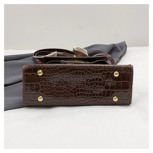 Close-up of dark brown crocodile texture bag bottom with four golden metal feet