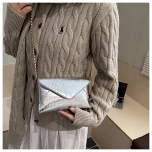 Detail of silver metallic envelope bag with wave texture on a beige knit cardigan