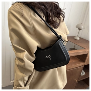 Detail of minimalist black shoulder bag with decorative silver bow metallic accessory