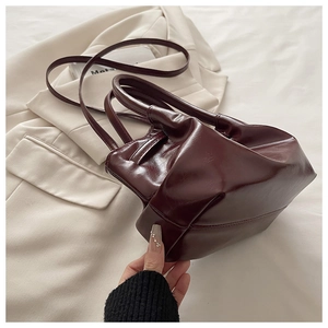 Detail of a dark brown glossy leather bucket bag with top handles and a slim shoulder strap