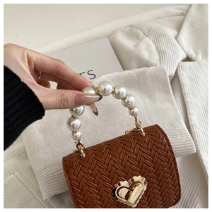 Detail of woven mini bag featuring pearl handle and golden heart lock on brown texture