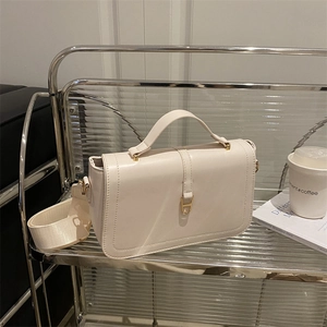 Minimalist beige crossbody bag with wide strap and gold horseshoe buckle on metal stand