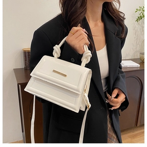 Detail of white PU leather handbag featuring gold metal trim and stylish knotted handle