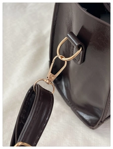 Close-up of golden metal lobster clasp on a glossy dark brown leather tote bag detail