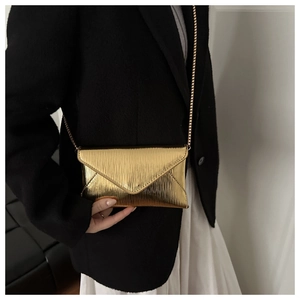 Detail of a metallic gold envelope clutch featuring a vertical striped texture and chain strap