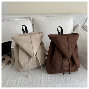 Close-up of bunny ear flap backpacks in beige and brown matte suede on a sofa