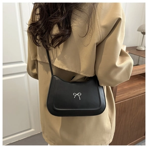 Detail of a black leather crossbody bag with a silver bow buckle on a trench coat