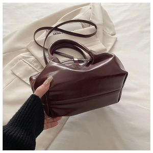 Detail of dark brown polished leather bucket bag with metal clasp and shoulder strap