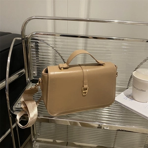 Minimalist khaki crossbody flap bag with wide fabric strap on a display shelf