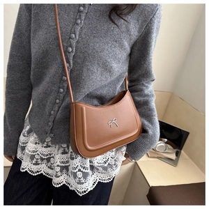 Detailed view of brown leather half-moon bag with silver bow ornament on model