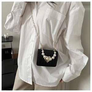 Detail of black woven crossbody bag with pearl handle and golden heart clasp on model
