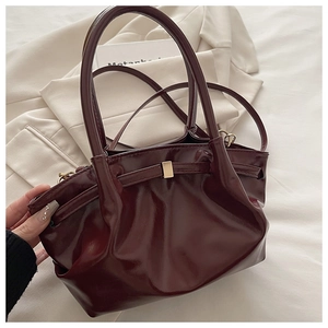 Detail view of burgundy pleated leather bucket bag with gold metal buckle on beige blazer
