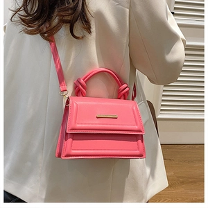 Detail of pink crossbody bag with a knotted handle and golden metal bar on the flap